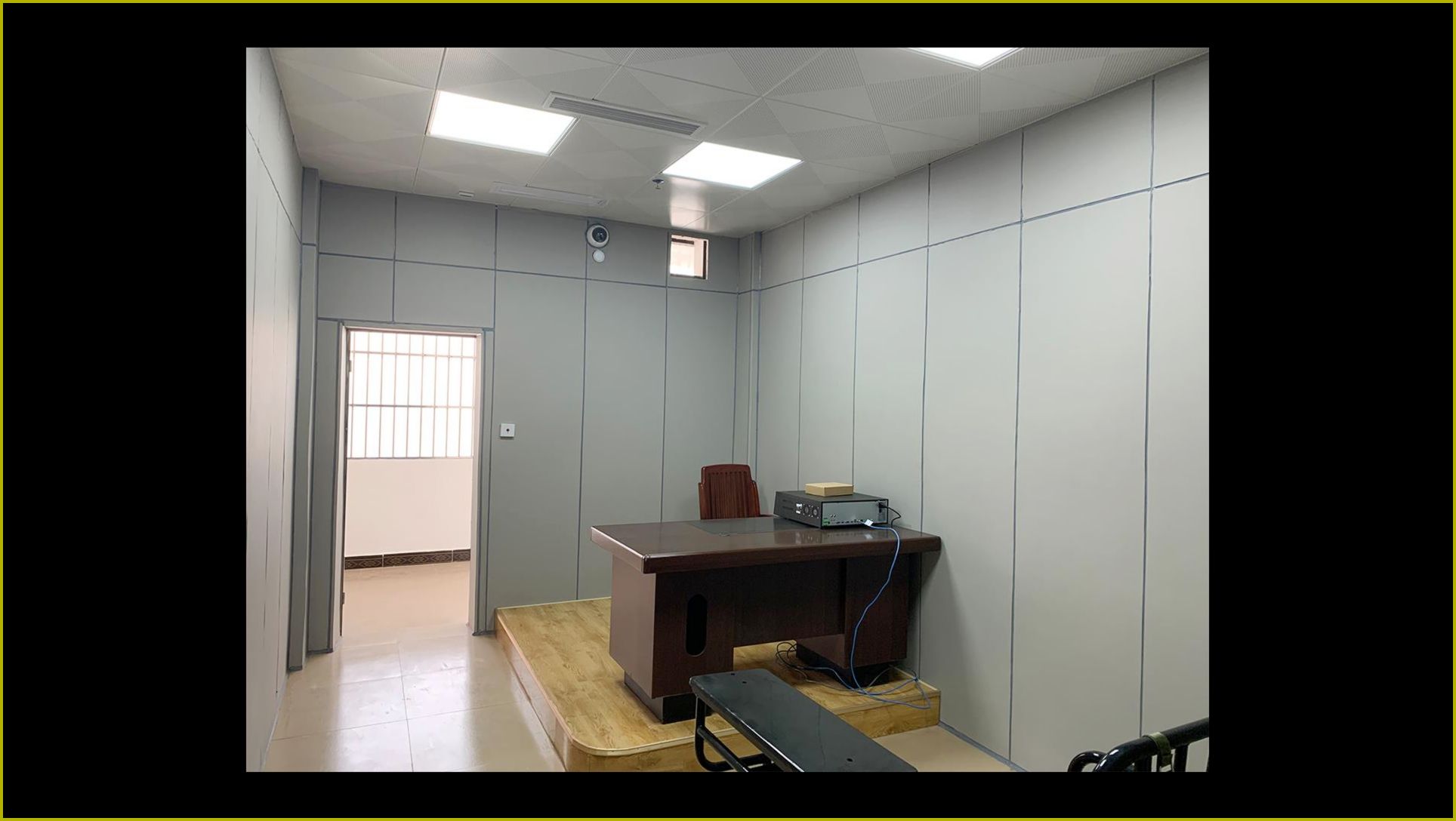 公安办案区审讯室防撞软包墙面整体装修实景，灰色软包墙板满铺搭配审讯桌椅
