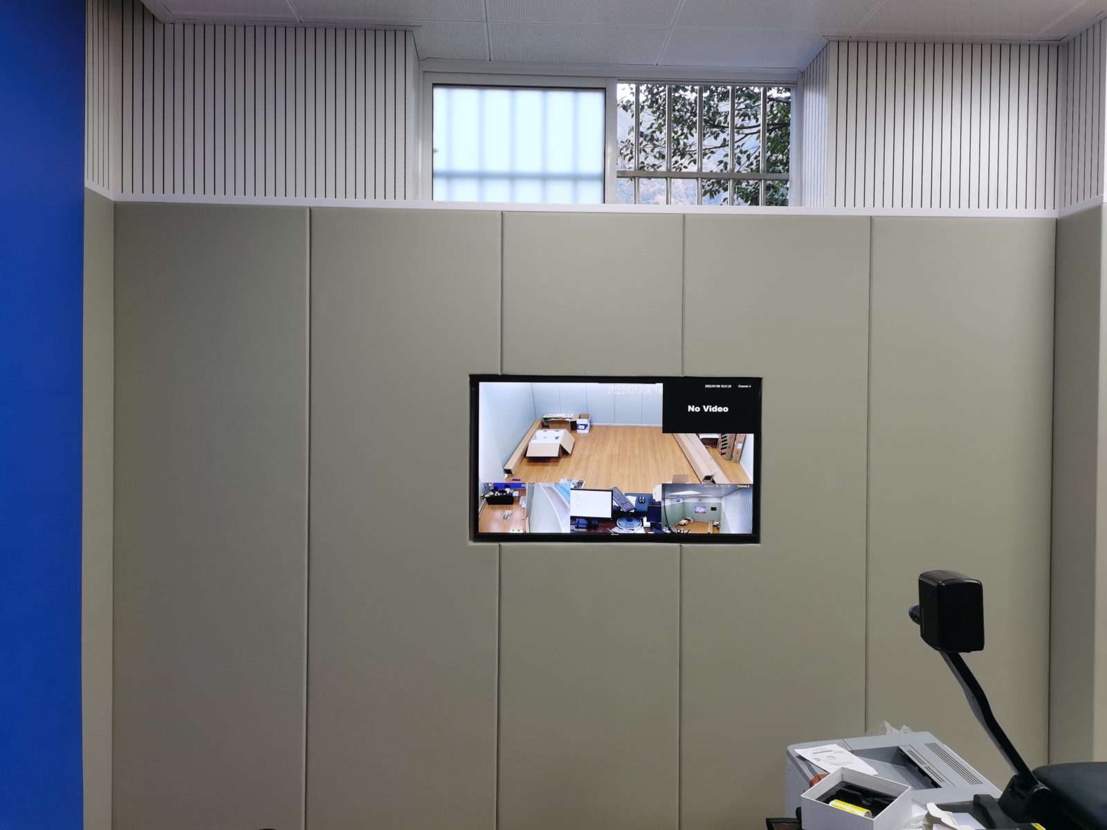 公检法办案区审讯室米色防撞软包墙面装修实景，嵌入监控显示屏，上部搭配白色木条吸音板防自伤设计