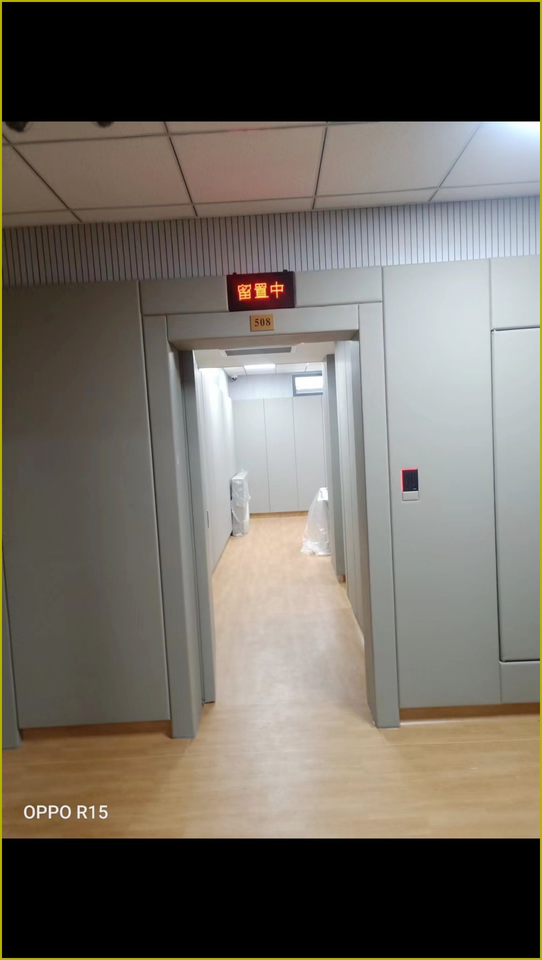 留置室走廊防撞软包墙面安装实景,灰色软包墙板搭配防撞门与门禁锁,适用于办案区防自伤设计