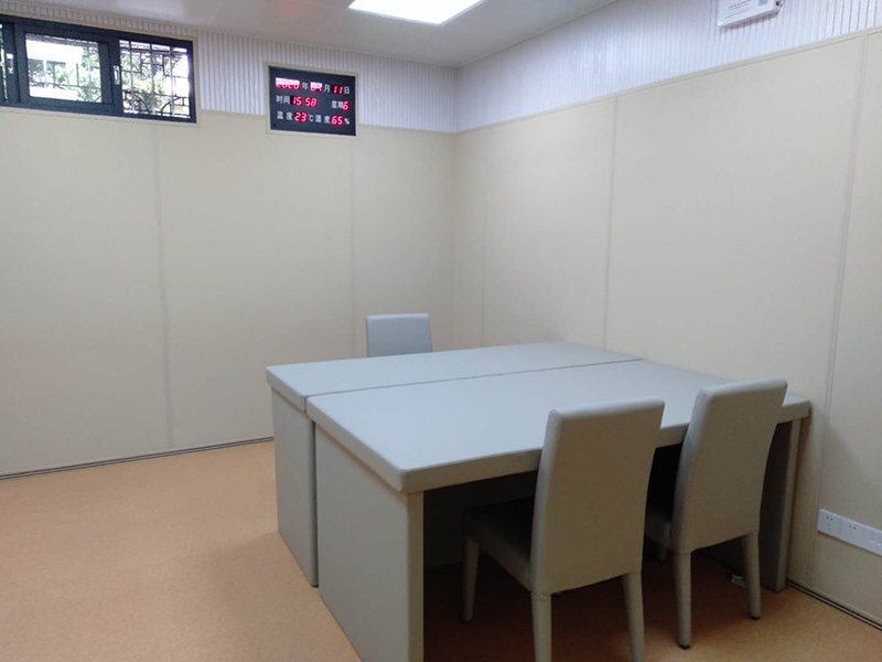 公检法办案区询问室防撞软包整体实景，米色软包墙面搭配圆角防撞桌椅与温湿度显示屏