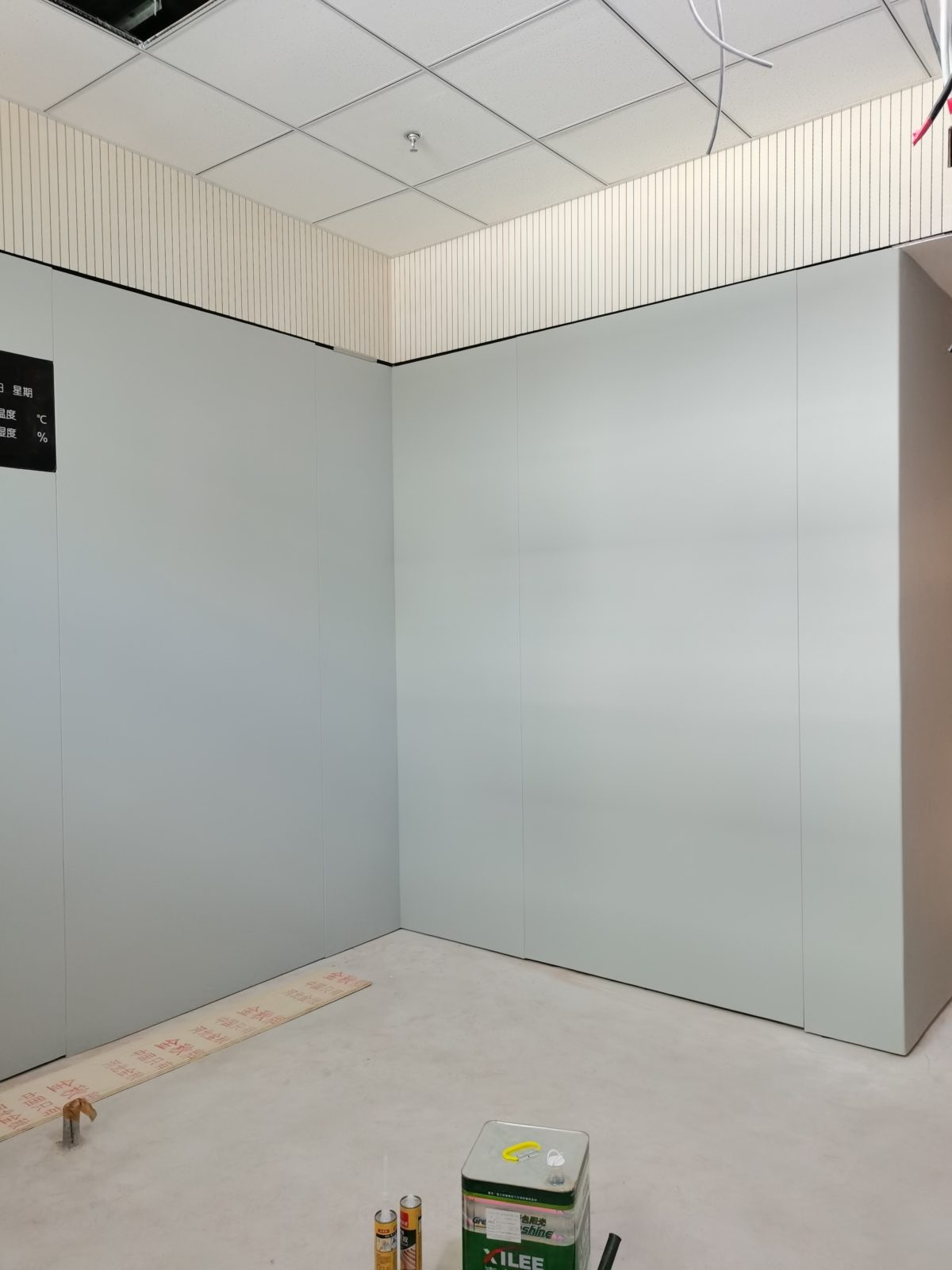 办案区审讯室灰色防撞软包墙面安装实景，顶部搭配木条吸音板与矿棉板吊顶