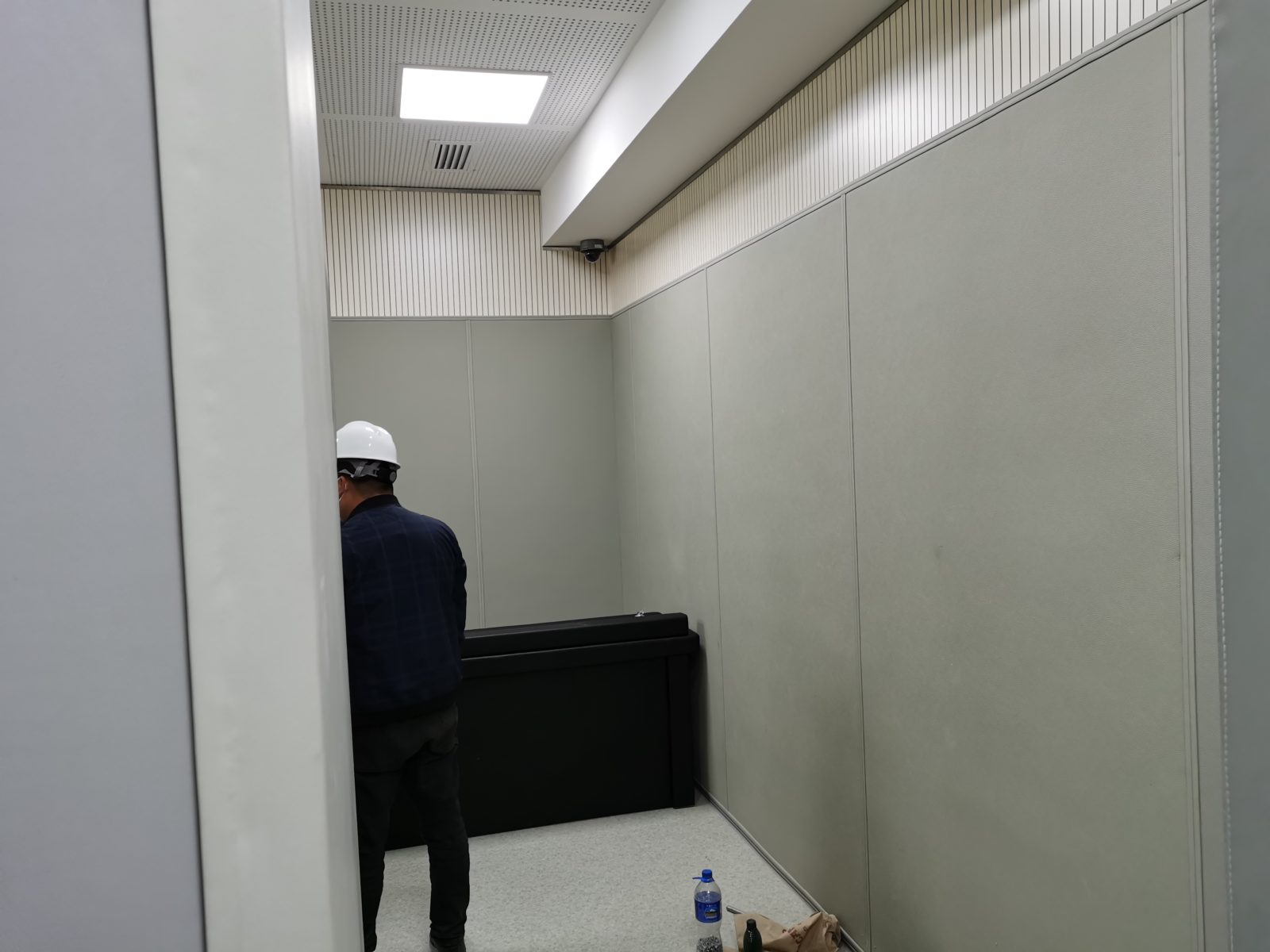办案区审讯室防撞软包墙面与防撞桌整体实景，灰色皮革软包墙板搭配槽木吸音板装饰