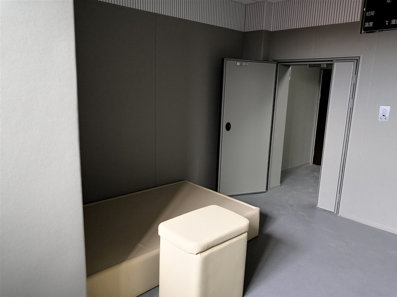留置室防撞软包整体装修实景，米色皮革软包墙面搭配防撞床与软包凳，配软包防撞门，防自伤设计
